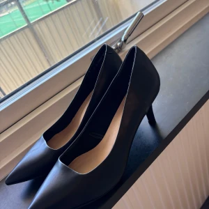 Nya Svarta pumps med spetsig tå  - Snygga svarta pumps från skopunkten med spetsig tå och låg klack. Skorna har en stilren och klassisk design i slätt syntetmaterial, perfekt för dig som gillar en elegant look. Passar dig som vill ha en tidlös och chic stil. Aldrig använt dom , säljer pgd av ej andvänt som