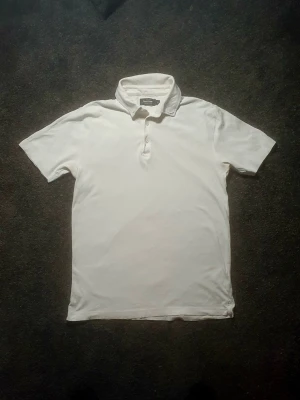 Vit pikétröja från Dressmann - Najs vit pikétröja från Dressmann i 100% Supima bomull (Premium linjen). Tröjan har korta ärmar, krage och knappar framtill. Har lite småskavanker men är ändå ett fett plagg