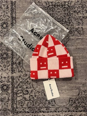 Rutig mössa från Acne Studios - Stickad mössa från Acne Studios i rött och ljusrosa. Perfekt accessoar för att lyfta din look nu under vintern. Helt ny bra pris skriv vid funderingar