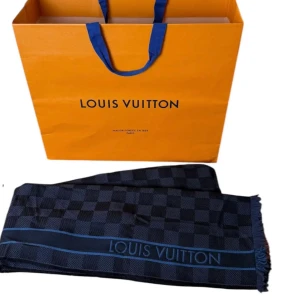 Louis Vuitton halsduk - Exklusiv halsduk från Louis Vuitton med klassiskt rutigt mönster i mörkblå och marinblå toner. Snygga detaljer med röda och grå ränder samt LV-logga. Halsduken har fransad kant och är tillverkad i mjukt material som känns lyxigt mot huden. 