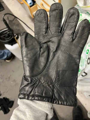 Svart skinnhandske fodrad - Säljer en klassisk svart skinnhandske med mjukt foder på insidan. Handsken har tre dekorativa sömmar på ovansidan och elastisk söm vid handleden för bättre passform. Tillverkad i Rumänien och perfekt för kalla dagar.