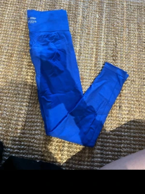 Blå träningstights med hög midja - Säljer ett par starkt blå träningstights från H&M med hög midja. De är tillverkade i stretchigt syntetmaterial som sitter tight och följer kroppen perfekt. Perfekta för gymmet eller löprundan!