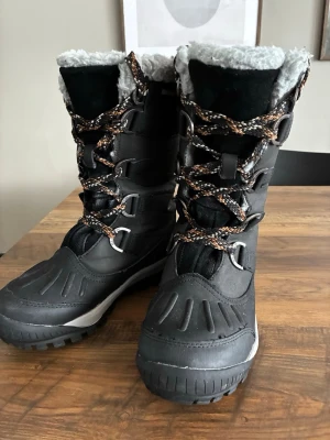 Vinterkänga Bearpaw  - Vattentäta varma vinterstövlar från Bearpaw tillverkade i skinn med plös i mocka. Ljusgrå skaftmudd i ull. Varmt fodrade med ullblandning och löstagbar sula i fårskinn. Platt snörning med D-ringar.  Minimalt använda. Liten i storlek. Storlek 37 men mer som än 36a