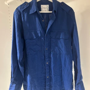 Blå overshirt/skjorta  från Replay - Snygg blå overshirt från Replay med klassisk krage, två stora bröstfickor med lock och axelklaffar. Skjortan har långa ärmar och knäppning framtill. Perfekt att bära öppen eller stängd för en cool look.