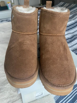 Bruna boots från Canada Snow - Säljer ett par bruna boots från Canada Snow med mjukt vitt foder och mocka på utsidan. Skorna har rund tå, platt sula och en rejäl yttersula med mönster för extra grepp. Perfekta för kalla dagar och har en klassisk, enkel design. 