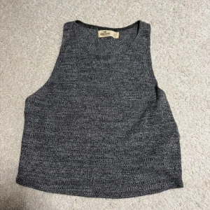 Mörkgrå ribbad linnetopp Hollister - Säljer en mörkgrå ribbad linnetopp från Hollister i storlek S. Toppen är croppad och ärmlös med en enkel, stilren design och rund halsringning. Perfekt att matcha med höga jeans eller kjol för en chill look.