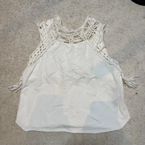 Vit boho linnetopp betternblue - Säljer en vit linnetopp från Better In Blue med boho-vibbar. Toppen har ett unikt makramé-mönster upptill och i ryggen, samt fransar längs nederkanten bak. Ärmlös och i mjukt bomullsmaterial. Perfekt till sommaren för en chill och trendig look.