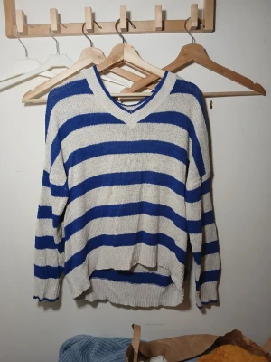 Randig stickad tröja med v-ringning - Säljer en stickad tröja med breda blå och vita ränder. Tröjan har v-ringad hals, lång ärm och en lite loose passform. 