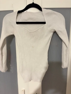 Vit ribbad långärmad topp - Säljer en vit ribbad topp med lång ärm och snygg v-ringad skärning. Tröjan är figurnära och har stretchigt material som sitter snyggt på kroppen. Perfekt till jeans eller kjol för en clean look.