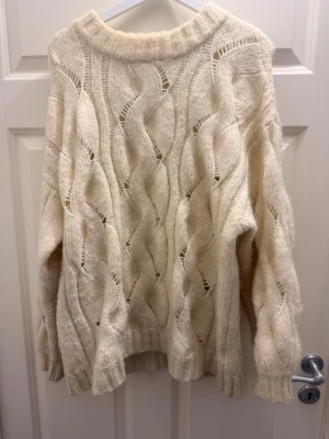 Beige stickad tröja med vågmönster - Säljer en oversized beige stickad tröja med vågiga detaljer och bred ribbad krage. Tröjan har lång ärm och ett luftigt, chunky mönster som ger en riktigt mysig vibe. Perfekt för lager på lager under kyliga dagar.