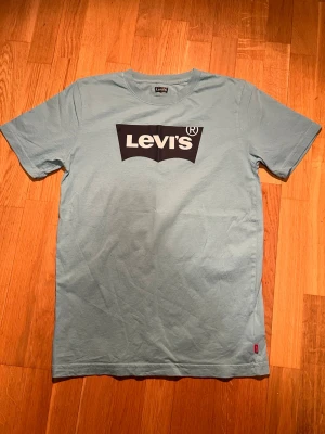 Turkos Levi's t-shirt med logga - Snygg turkos t-shirt från Levi's med klassisk svartvit logga på bröstet. T-shirten har korta ärmar och rund halsringning. Tillverkad i mjuk bomull för skön känsla och enkel stil.