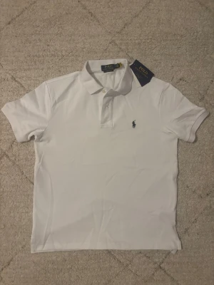 Pikétröja Ralph Lauren - Helt ny vit pikétröja från Ralph Lauren, aldrig använd och med lapparna kvar. Klassisk och tidlös modell i högkvalitativt material som ger en stilren och fräsch look. Storlek M, passar mig perfekt som är 178 cm (Jag på bilderna). Modellen är ”Slim-fit” och är en bekväm och snygg passform, varken för tight eller för lös. Om du har några frågor alls tveka inte att skriva!