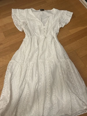 Vit spetsklänning med volangärm - Säljer en vit klänning i spets med v-ringning och knappar framtill. Klänningen har volangärmar och ett lätt utställt fall. Materialet är spets med fina detaljer och klänningen har en mjuk underklänning. Perfekt för sommarens alla tillfällen! Pris kan diskuteras 