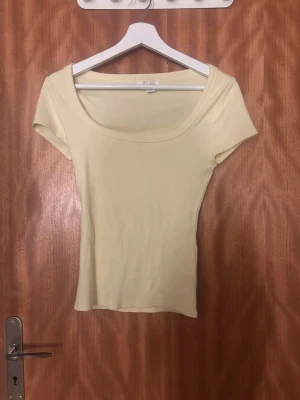 Ljusgul topp från Amisu - En ljusgul, ribbad topp från Amisu med korta ärmar och rundad, djup urringning. Perfekt att styla med jeans eller kjol för en fräsch look. Enkel och stilren design som passar till många outfits. Är i ett nytt skick bara utom prislapp