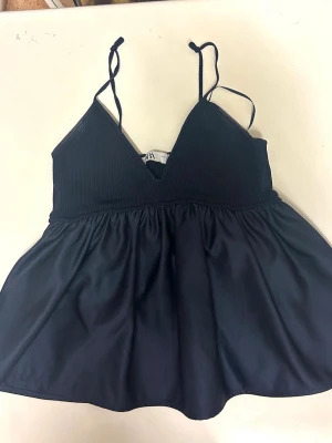 Marinblå Zara topp - Snygg marinblå linnetopp med smala axelband och v-ringad hals. Toppen har en ribbad överdel och ett lätt utställt fall nedtill. Perfekt att styla med jeans eller kjol för en trendig look.
