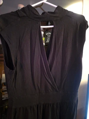 Svart omlottklänning från KappAhl - Svart omlottklänning från KappAhl med djup v-ringning och ärmlös design. Klänningen har markerad midja och ett mjukt, följsamt tyg som ger en snygg siluett. Perfekt för dig som gillar stilrena och klassiska plagg.