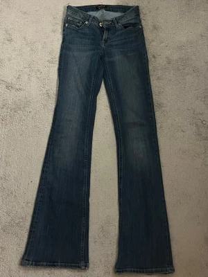 Blå bootcut jeans med låg midja - Snygga blå jeans med bootcut-modell och låg midja. Jeansen har klassisk femficksdesign och är tillverkade i ett mjukt denimtyg. Perfekta för dig som gillar en retroinspirerad look med utsvängda ben. ( se bild 4 för ett litet hål som är ovanför vänster bakficka )