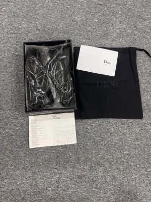 Svarta Dior sneakers med vita detaljer - Helt nya aldrig använda kommer med kvitto köpts utomlands, box kvitto skor allt ingår Snygga svarta Dior sneakers med vita kontrastsömmar och logga på sidan. Skorna har snörning och en chunky platt sula för en modern look. Tillverkade i syntetmaterial och levereras med originalpåse och kort från Dior.