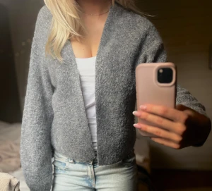 Grå mjuk kofta - Säljer en mysig grå kofta med v-ringning och lång ärm. Koftan är i ett fluffigt, stickat material och har en avslappnad passform. Perfekt att slänga över en topp för en chill look.