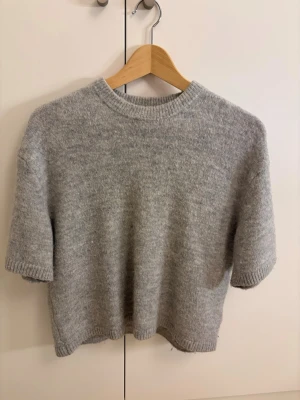 Grå stickad tröja Gina Tricot - Mjuk och enkel grå stickad tröja från Gina Tricot med korta ärmar och rund hals. Tröjan har ribbade muddar vid hals, ärmslut och är mycket skön! Tröjan har inga skador!!