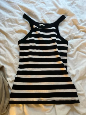 Randig ribbad linnetopp svart/vit - Säljer en snygg ribbad linnetopp med breda svarta och vita ränder. Toppen är ärmlös med breda axelband och har en tight passform. Perfekt för dig som gillar en enkel men trendig stil.