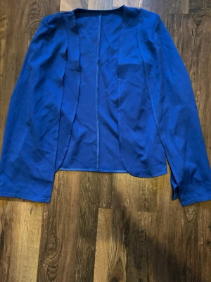 Blå kavaj med cape-ärmar - Blå kavaj med unika cape-ärmar. Kavajen är öppen framtill och har en figurnära passform. Köparen står för frakten! 