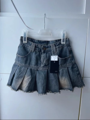 Denim kjol från CRYX - köpt i Japan - Aldrig använd jeanskjol från japanska märket CRYX. Kort modell med fransad kant, fickor och knäppning fram. Märkt S men har små mått – passar XS bäst. Unik design med vintage och streetwear-vibe. Perfekt för dig som gillar japanskt mode, edgy denim och stil med attityd.