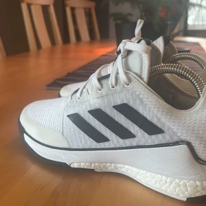 Adidas Crazyflight vita sneakers - Säljer snygga Adidas Crazyflight sneakers i vitt med svarta detaljer och klassiska tre ränder på sidorna. Ovandel i mesh och syntet, snörning framtill och stötdämpande sula med svart yttersula. Perfekta för dig som gillar sportig stil eller går på någon sport, kan användas till allt så som, idrott i skolan innebandy, tennis, basket med mera. Skick:9/10 använda inte alls länge. Ny pris: 1700kr mitt pris: 680kr
