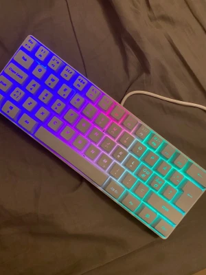 RGB-belyst kompakt tangentbord - Säljer ett kompakt tangentbord med RGB-belysning som lyser i flera färger som blått, rosa och grönt. Tangentbordet är vitt och ansluts med kabel. Perfekt för dig som vill ha en snygg setup till datorn.