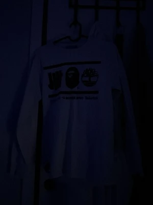 Vit långärmad tröja med tryck (bape tröja)  - Vit långärmad tröja med svart tryck framtill som visar olika loggor och text. Rund halsringning och rak passform. Perfekt för en avslappnad streetwear-look.  skriv ifall du är intresserad så kan vi prata om priset 