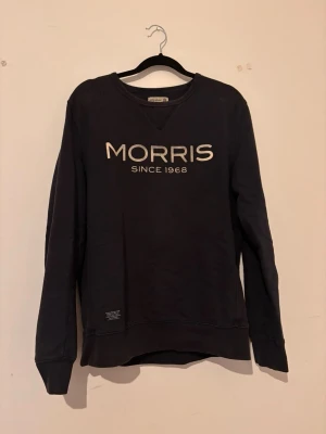 Svart sweatshirt från Morris - Cool svart sweatshirt från Morris med trycket 'MORRIS SINCE 1968' i vitt på bröstet. Klassisk rund halsringning och långa ärmar. Perfekt för en avslappnad och stilren look. Tillverkad i mjukt bomullsmaterial.