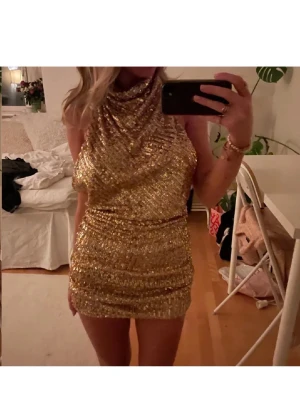 Glittrig guld kortklänning stl xs zara - Säljer en glittrig kort klänning i guld med paljetter. Klänningen har hög hals och är ärmlös, med en tight passform och öppen i ryggen. Perfekt för dig som vill sticka ut och glänsa på nästa fest! ✨Stl xs från Zara.                                         OBS! Halterneck med tre knappar, en är trasig, inget som syns eller påverkar klänningen!  Skriv vid funderingar eller fler bilder!🥰🥰