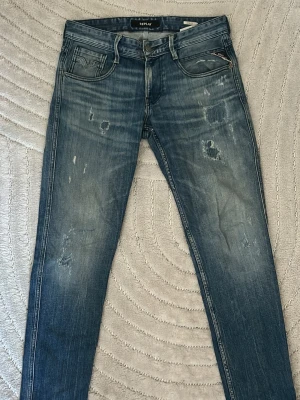 Replay blå slitna jeans skinny fit - Säljer ett par blå skinny jeans från Replay med slitningar och snyggt tvättad look. Jeansen har klassisk femficksmodell, låg midja och detaljerade sömmar. Perfekta för dig som gillar en avslappnad men trendig stil.