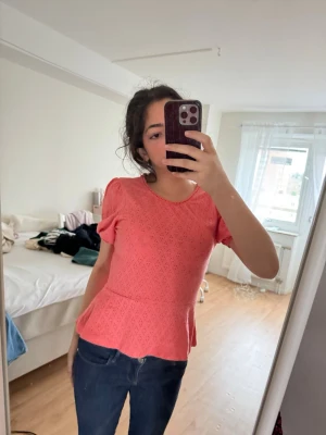Coral  blus med volang  - Supersöt rosa blus från Lindex med korta puffärmar och volang nertill. Blusen har ett diskret hålmönster och rund halsringning. Perfekt för dig som gillar en feminin och trendig stil. Storlek xs och är helt ny med etiket. 