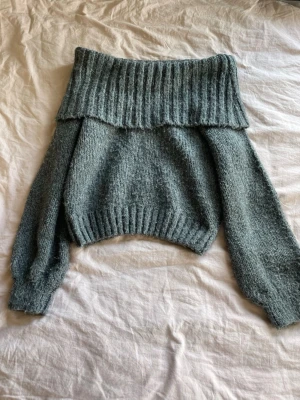 Grå stickad off shoulder-tröja - Mysig grå stickad tröja med bred ribbad off shoulder-krage och långa ärmar. Tröjan har en avslappnad passform och ribbade muddar vid ärmslut och nederkant. Perfekt för lager-på-lager och chill dagar.