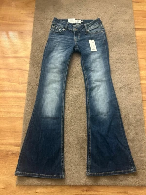 Blå  Super low Rise bootcut jeans från lager 157 - Helt nya snygga blå bootcut jeans från Lager 157 med ljusa slitningar framtill. Jeansen har normal passform upptill och vida ben från knät och ner. Perfekta för dig som gillar retrovibbar och vill ha ett par jeans som sticker ut.