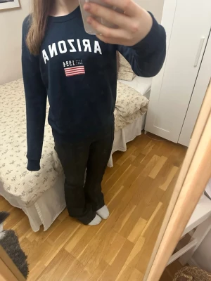 Mörkblå stickad tröja Arizona - Mörkblå stickad tröja med trycket 'ARIZONA 1994' och en liten amerikansk flagga på bröstet. Tröjan har rund halsringning och långa ärmar. Perfekt för dig som gillar college-stil och vill ha en enkel men snygg look.