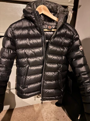 Svart dunjacka från Colmar - Snygg svart dunjacka från Colmar med huva. Den är i bra skick dock så finns de ett hål på ryggen. Jackan är tjock och varm och funkar till de mesta, vet dock inte vilken storlek 44 är men skulle säga att jackan är i storlek S