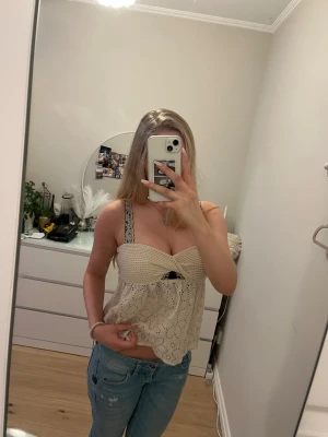 Beige tub topp - Supersöt beige tub topp med broderade blommor och twistad detalj framtill. Toppen är axelbandslös och har en luftig passform, perfekt för varma dagar. Materialet känns som bomull och ger en romantisk vibe. Storleken är XS men passar även S