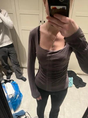 Brun/grå långärmad topp med drapering - Säljer en brun/grå långärmad topp med snygg drapering och bred, rundad urringning. Toppen har en tight passform och är gjord i mjuk bomullsmix som sitter skönt mot kroppen. Pris diskuteras gärna! 