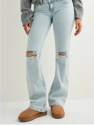 Nelly Jeans - Snygga ljusblå bootcut jeans med slitningar över knäna och broderade detaljer på bakfickorna. Jeansen är low waisted. Använda men inga tecken på det, inga defekter och allt är som det ska! Säljer då de inte längre kommer till användning. Nypris: 700kr