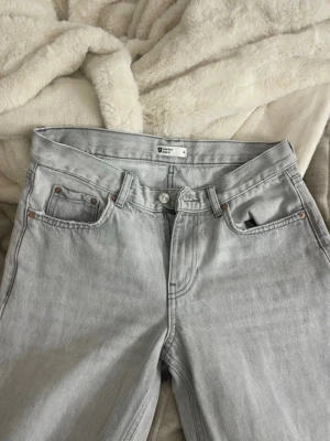 Ljusgrå raka jeans från Gina Tricot - Säljer ett par ljusgrå jeans från Gina Tricot med klassisk femficksmodell och raka ben. Jeansen har bälteshällor, knappgylf och är tillverkade i mjukt bomullsjeans-tyg. Perfekta för en avslappnad och trendig look. Inte använda på ett tag. Storlek 36 
