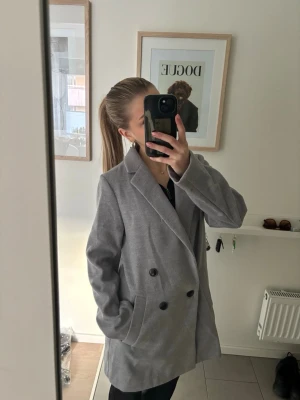 Grå kappa från H&M - Stilren grå kappa från H&M med dubbelknäppning och klassisk krage. Kappan har två fickor framtill och en rak passform som passar perfekt till vardagslooken. Enkel att matcha med olika outfits och funkar året runt. Lite tunnare så perfekt till våren!