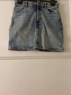 Ljusblå jeanskjol i klassisk modell - En ljusblå jeanskjol med klassisk femficksdesign och rak passform. Kjolen har bälteshällor och stängs med knapp och dragkedja framtill. Perfekt till sneakers eller boots för en avslappnad look. Bara att fråga ifall du undrar något eller behöver fler bilder! Pris kan diskuteras 💞