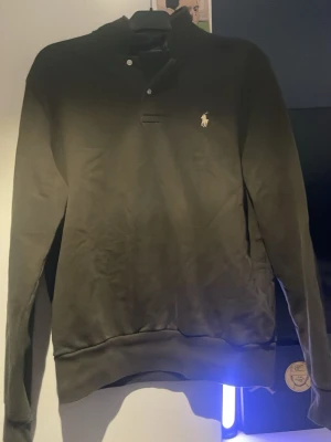 Mörkgrön tröja från Polo Ralph Lauren - Snygg mörkgrön långärmad tröja från Polo Ralph Lauren med klassisk krage och knappslå. Tröjan har den ikoniska loggan broderad på bröstet och är tillverkad i mjukt bomullsmaterial. Perfekt för en stilren och avslappnad look.priset är inte hugget i sten!!!!!!!!