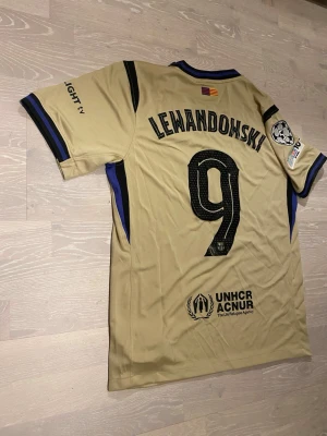 Beige Barcelona 25/26 T-shirt  Lewandowski  - •Hej! Säljer en jätte snygg Beige Barcelona 25/26 fotbolls T-shirt med Lewandowski på ryggen ⚽️👕 •Den är inte använd bara testad.  •Det är storlek M och den har inga hål eller liknande. •Måtten är på dem sista bilderna 📐.  •Priset kan diskuteras och skickar inom 24 Tim😊💨