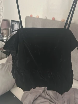 Svart sammetslinne med volang - Supersnygg svart linnetopp i sammet med smala axelband och volang nertill. Perfekt att styla med jeans eller kjol för en trendig look. Enkel och stilren design som passar till många outfits.