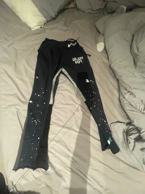 Svarta mjukisbyxor Gallery Dept. - Säljer ett par svarta mjukisbyxor från Gallery Dept. med vitt tryck på vänster höft och unika färgstänk över hela byxorna. Byxorna har resår i midjan med dragsko och raka ben. Perfekta för en avslappnad och trendig stil.