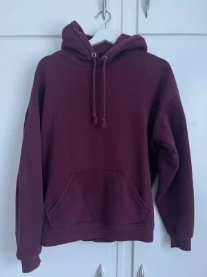 Vinröd oversized hoodie - Säljer en vinröd oversized hoodie med huva och dragsko. Hoodien har en stor magficka och ribbade muddar vid ärmslut och nederkant. Perfekt för en chill och avslappnad stil. Materialet känns mjukt och skönt mot huden.