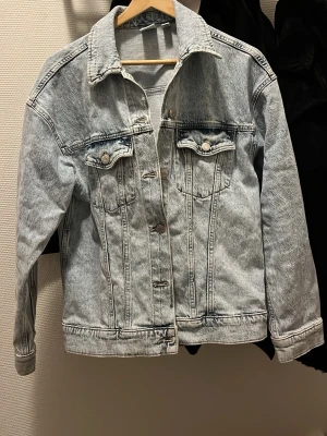 Ljusblå jeansjacka från Vero Moda - Snygg ljusblå jeansjacka från Vero Moda med klassisk krage, bröstfickor med knappar och raka sömmar. Jackan har långa ärmar och silverfärgade knappar framtill. Perfekt att slänga över en hoodie eller t-shirt för en chill look.